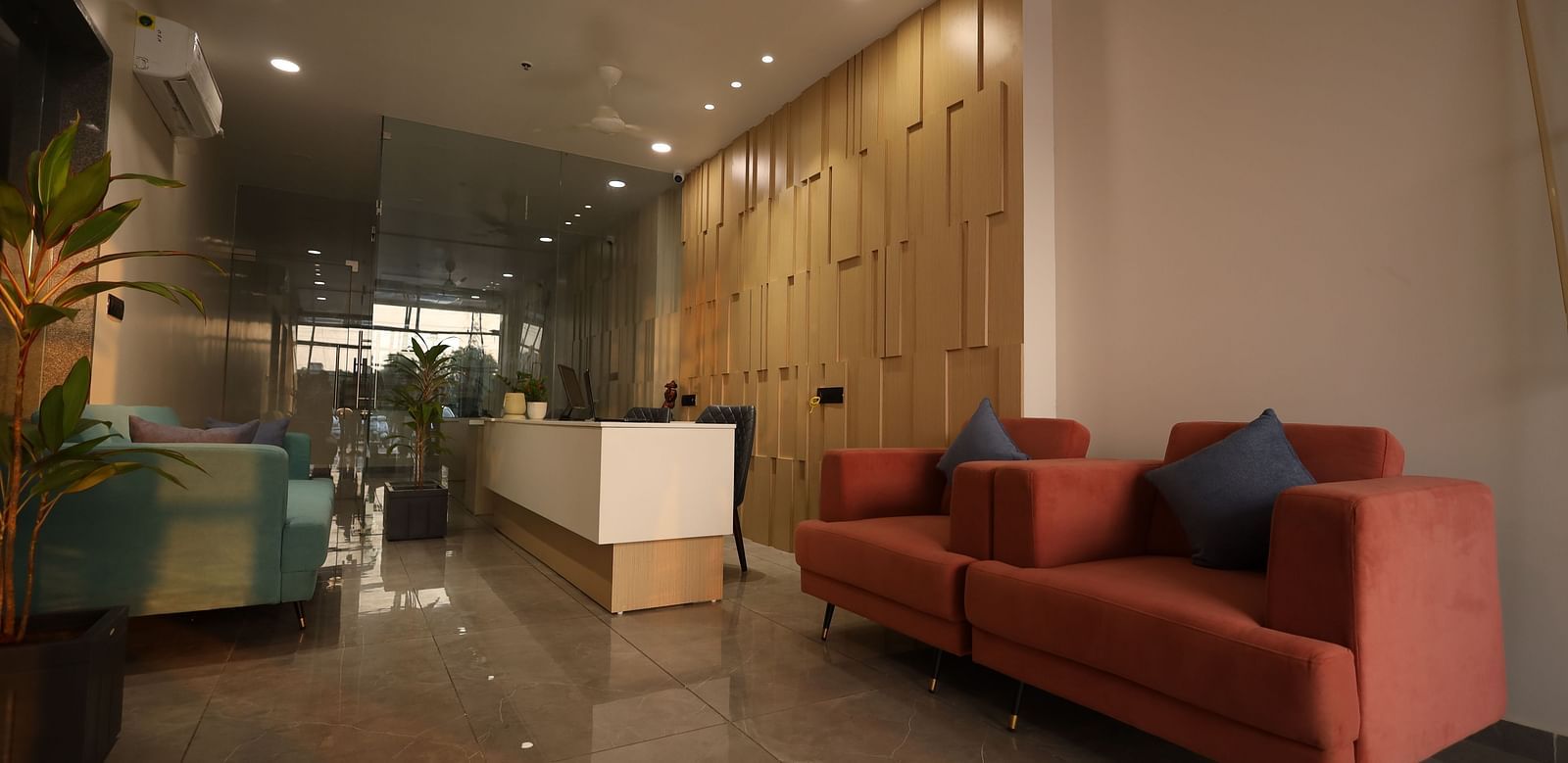 The image shows a reception or waiting area with sofas, a front desk, and a potted plant - Lords Eco Inn Navsari.