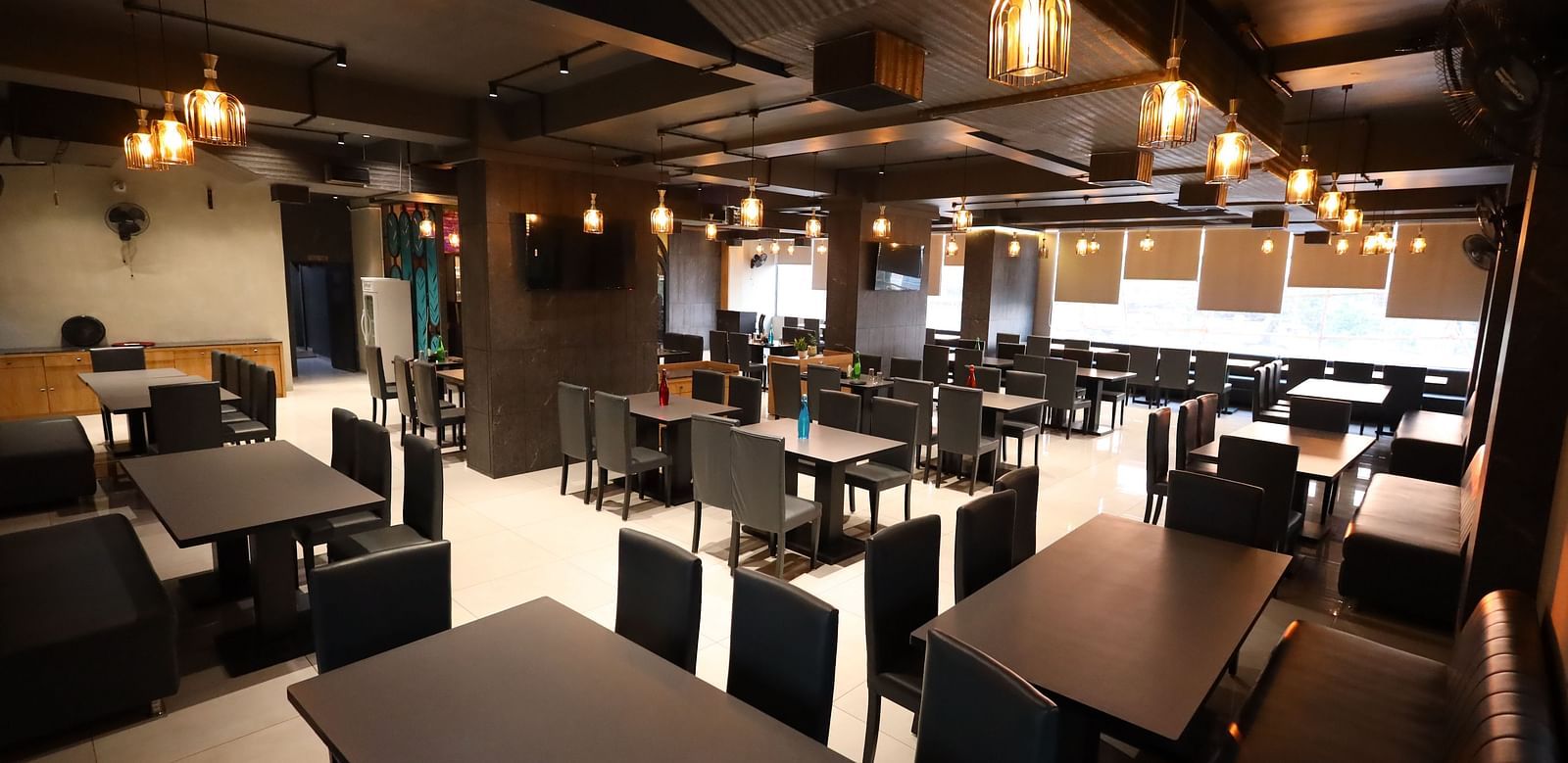 The image shows the interior of a restaurant with multiple tables and chairs under warm lighting - Lords Eco Inn Navsari.