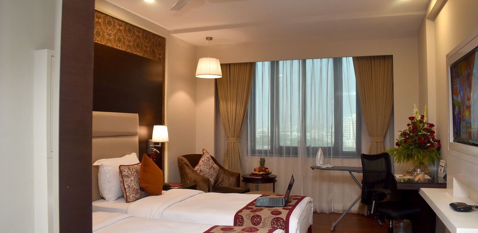 A hotel room with a bed, desk, and chair near a window at Lords Plaza Surat.