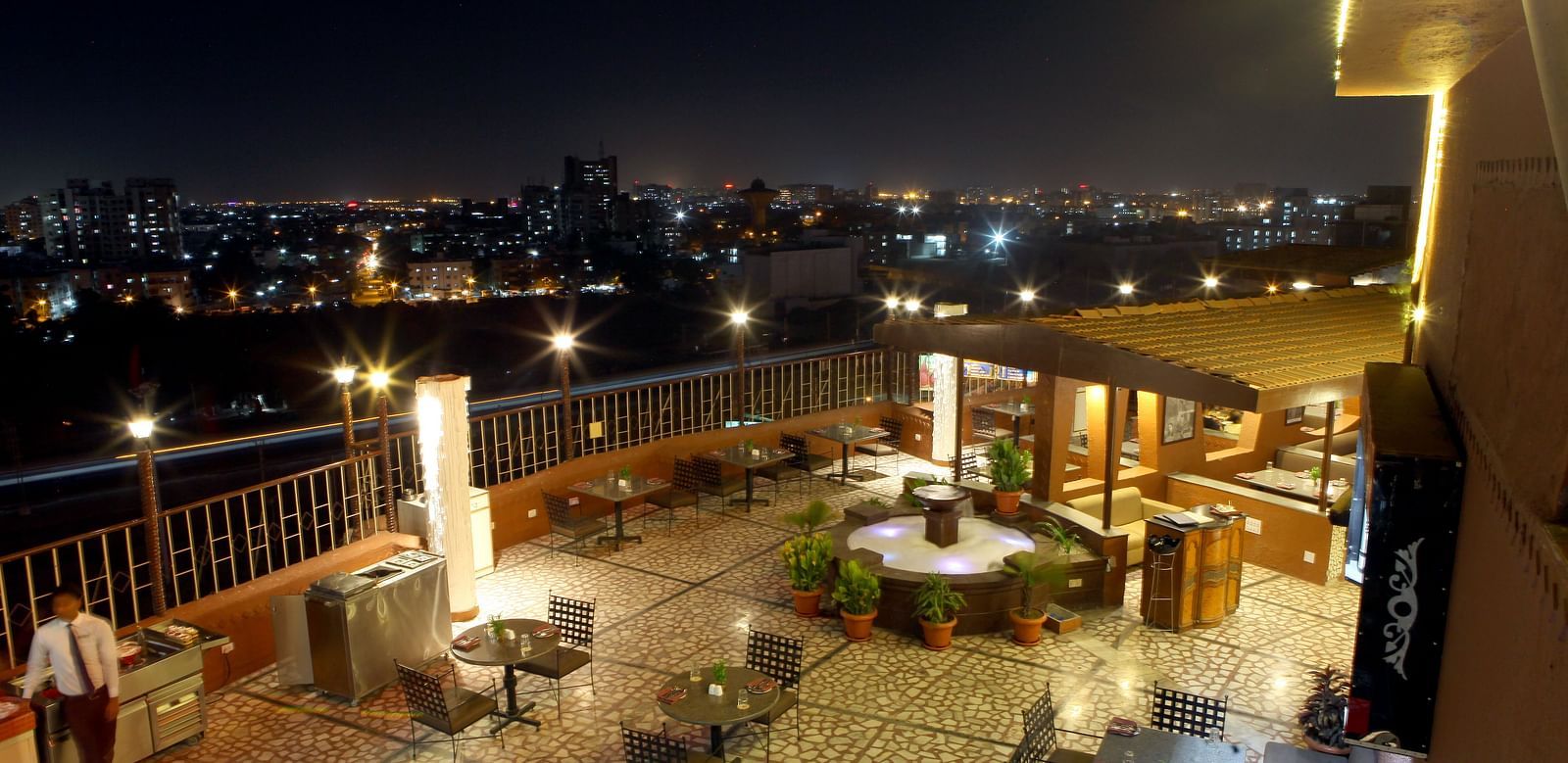 An outdoor seating area with city lights visible at night at Lords Plaza Surat.