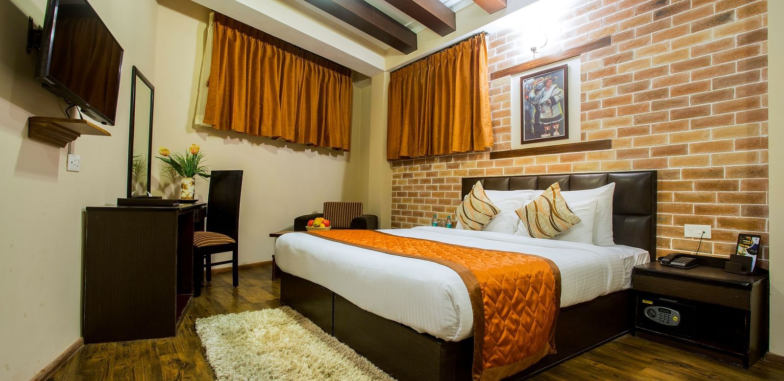 A hotel room at New Orchid Lords Inn Gangtok features a bed, desk, TV, and exposed brick wall.