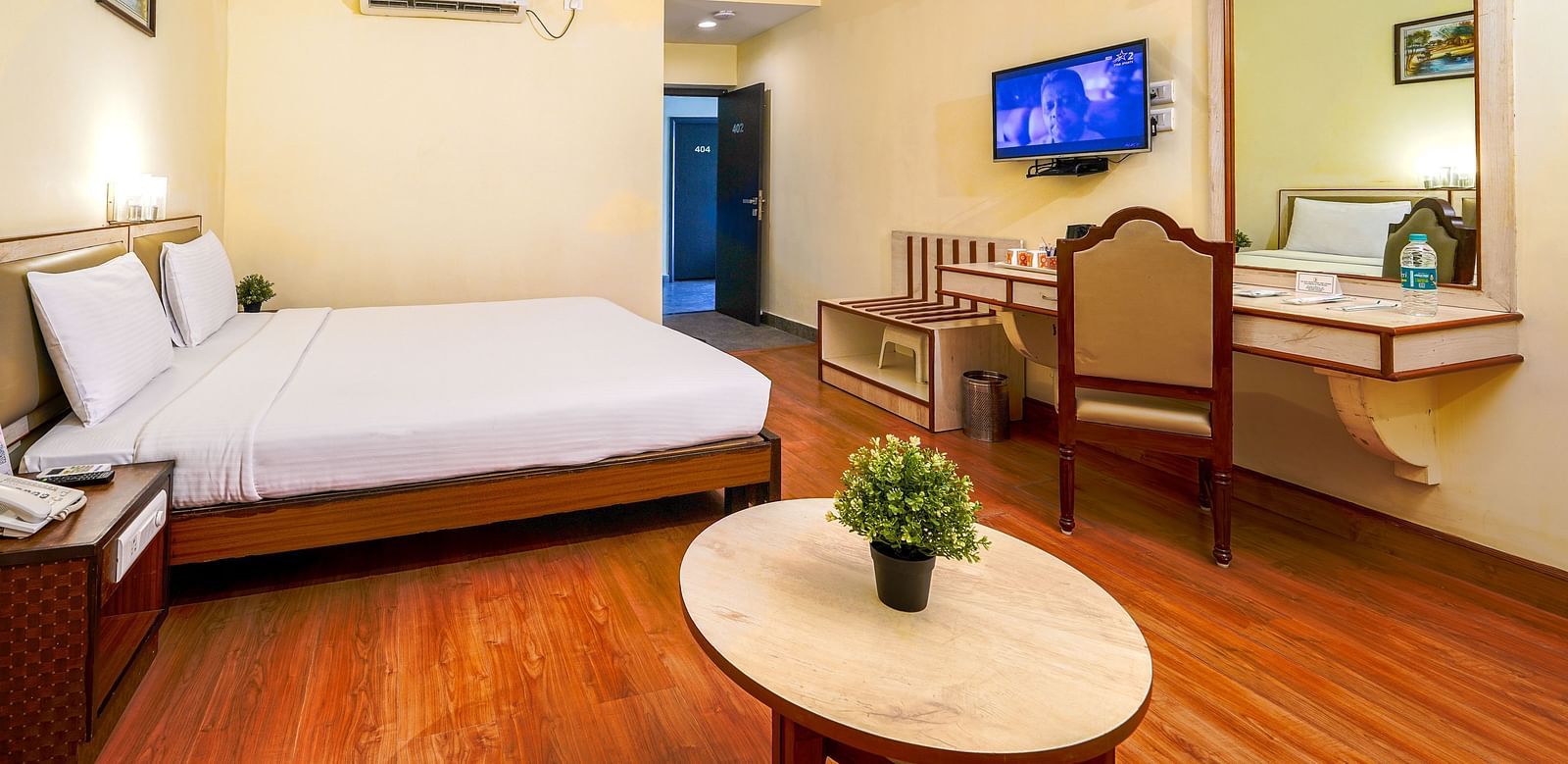 Spacious hotel room with a double bed, wooden flooring, flat-screen TV, and work desk in Hyderabad near Ramoji Film City.