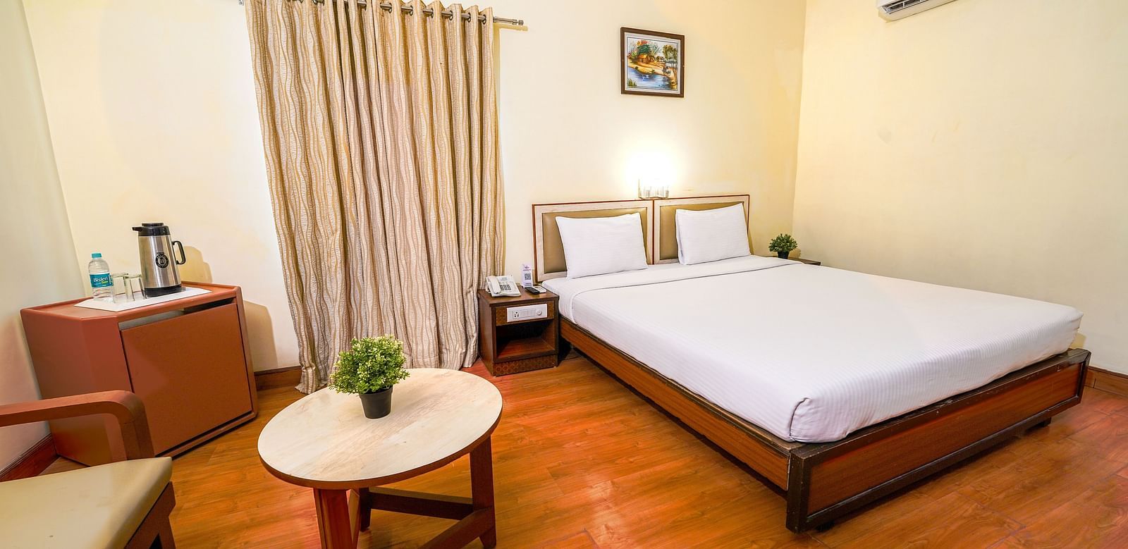 Bright hotel room with a double bed, wooden flooring, and a seating area by the window in Hyderabad near Ramoji Film City.