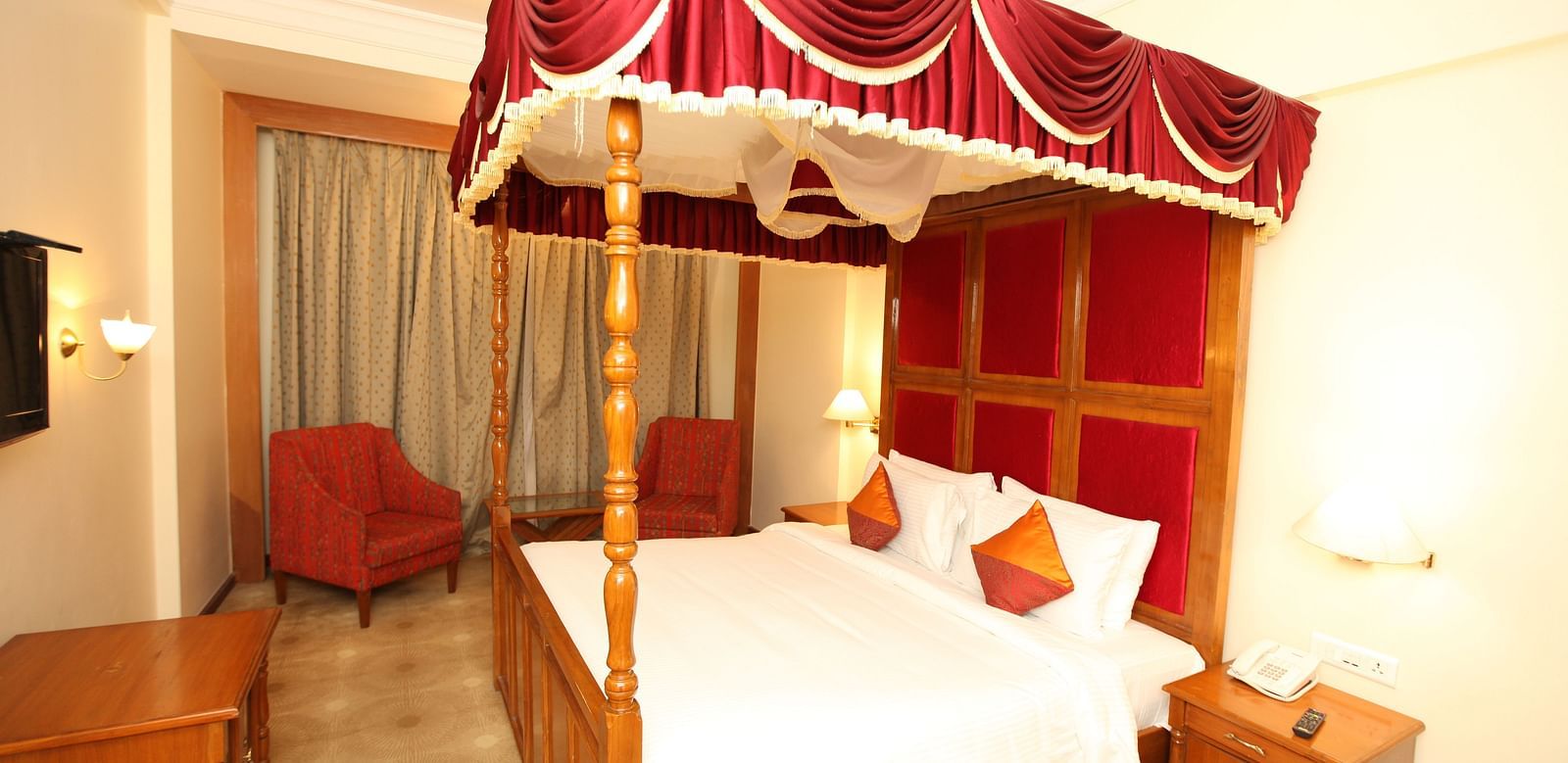 A luxurious hotel room with a red canopy bed, highlighting comfort and opulence at  Sitara Luxury Hotel in Hyderabad near Ramoji Film City.