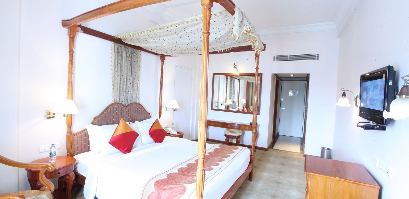 A well-lit hotel room with a four-poster bed, elegant decor, and ample space for relaxation at  Sitara Luxury Hotel in Hyderabad near Ramoji Film City.