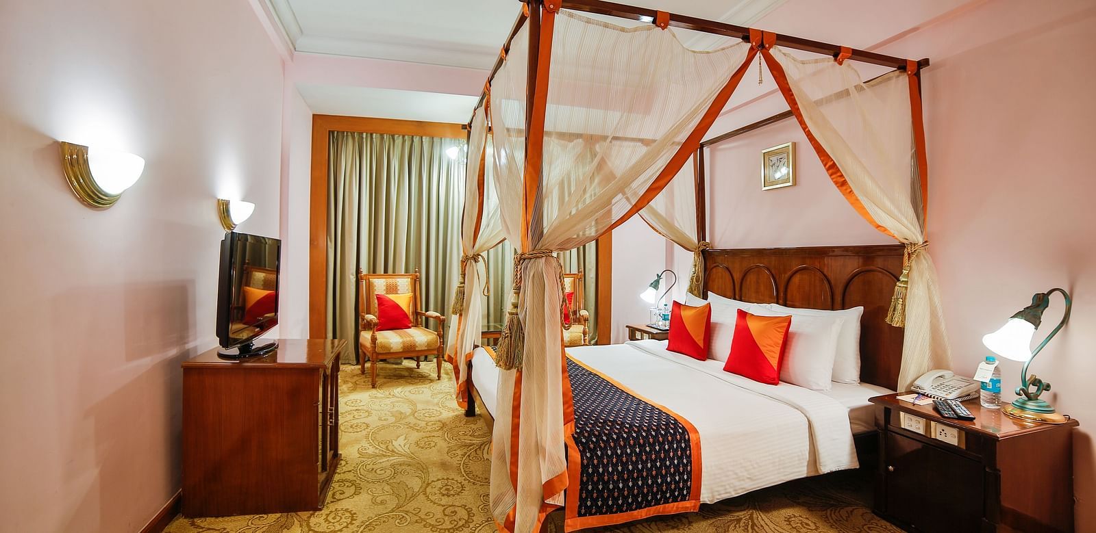 A spacious hotel room with a four-poster bed draped in sheer curtains, providing a serene atmosphere at  Sitara Luxury Hotel in Hyderabad near Ramoji Film City.