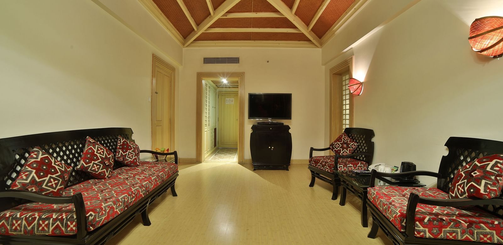 A hotel lounge area with traditional wooden sofas, patterned cushions, and a welcoming, open space A grand hotel suite with an opulent red and white decor, large bed, and seating area, reflecting a traditional style at Sitara Luxury Hotel in Hyderabad near