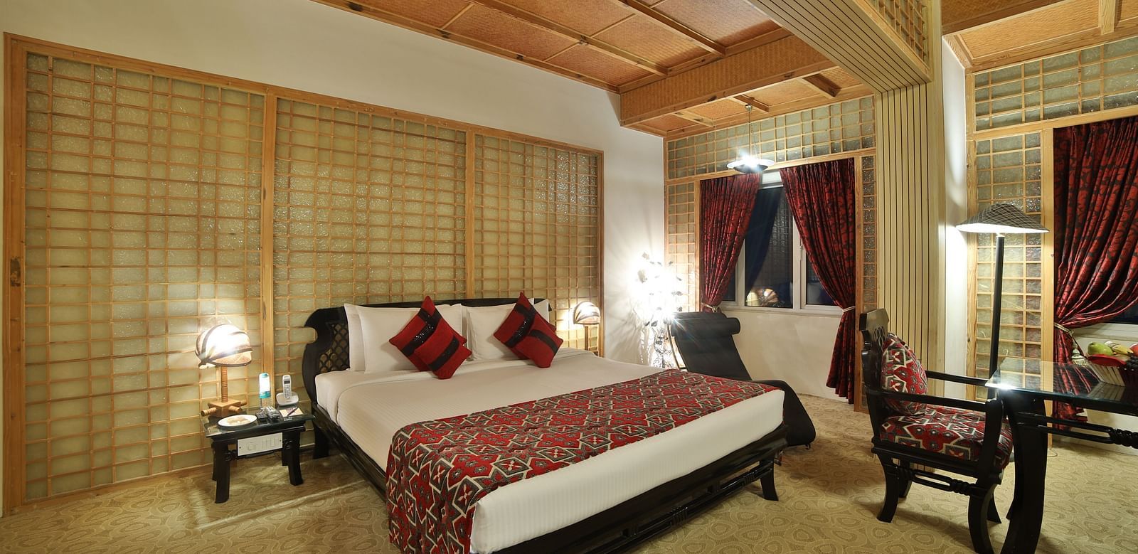 A luxurious hotel room with a richly patterned bedspread, elegant wooden furniture, and warm lighting A grand hotel suite with an opulent red and white decor, large bed, and seating area, reflecting a traditional style at Sitara Luxury Hotel in Hyderabad n