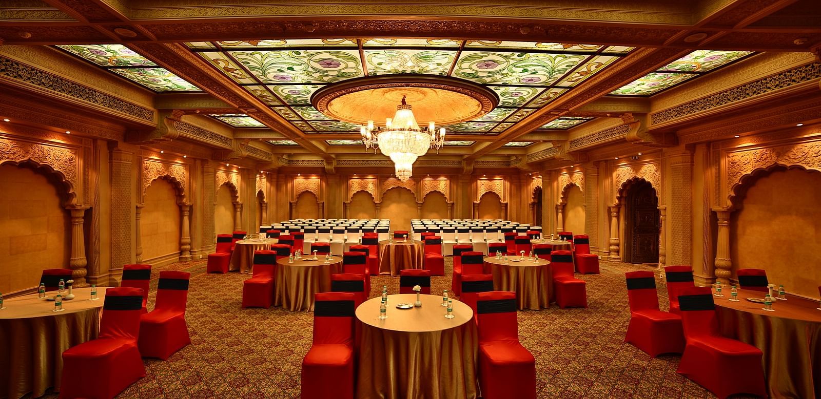 Seating arrangement in Taj Mahal Hall A grand hotel suite with an opulent red and white decor, large bed, and seating area, reflecting a traditional style at Sitara Luxury Hotel in Hyderabad near Ramoji Film City.