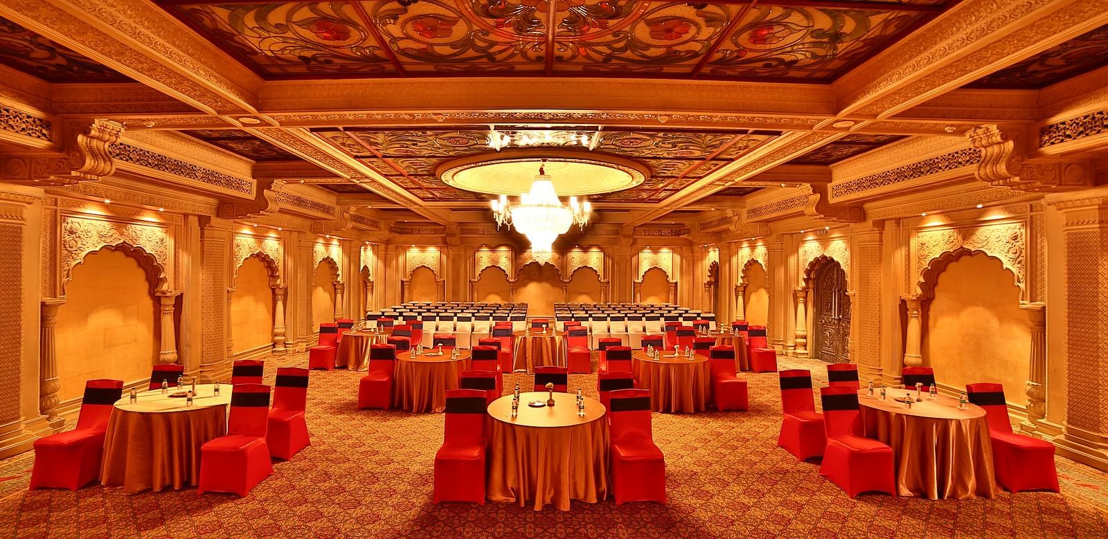 Seating arrangement in Taj Mahal Hall A grand hotel suite with an opulent red and white decor, large bed, and seating area, reflecting a traditional style at Sitara Luxury Hotel in Hyderabad near Ramoji Film City.