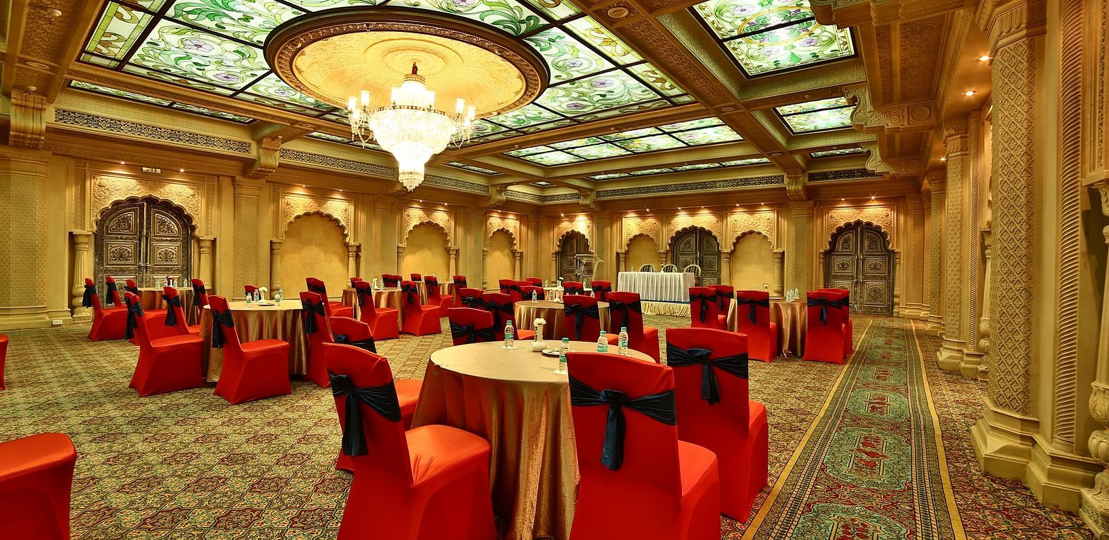 Seating arrangement in Taj Mahal Hall A grand hotel suite with an opulent red and white decor, large bed, and seating area, reflecting a traditional style at Sitara Luxury Hotel in Hyderabad near Ramoji Film City.