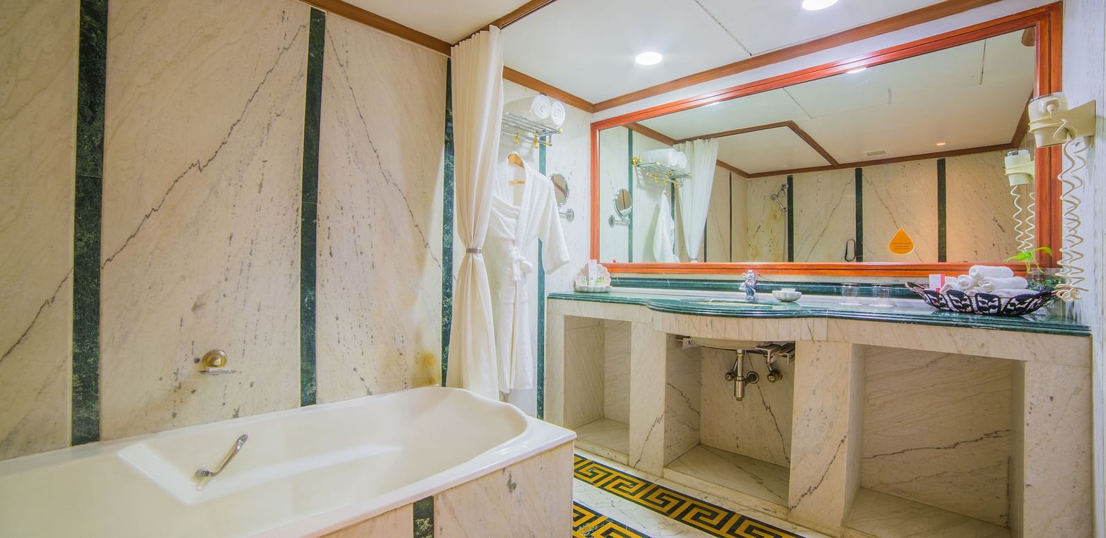 A spacious bathroom with a marble countertop, large mirrors, and a hint of traditional design in the tiling at Sitara Luxury Hotel in Hyderabad near Ramoji Film City.