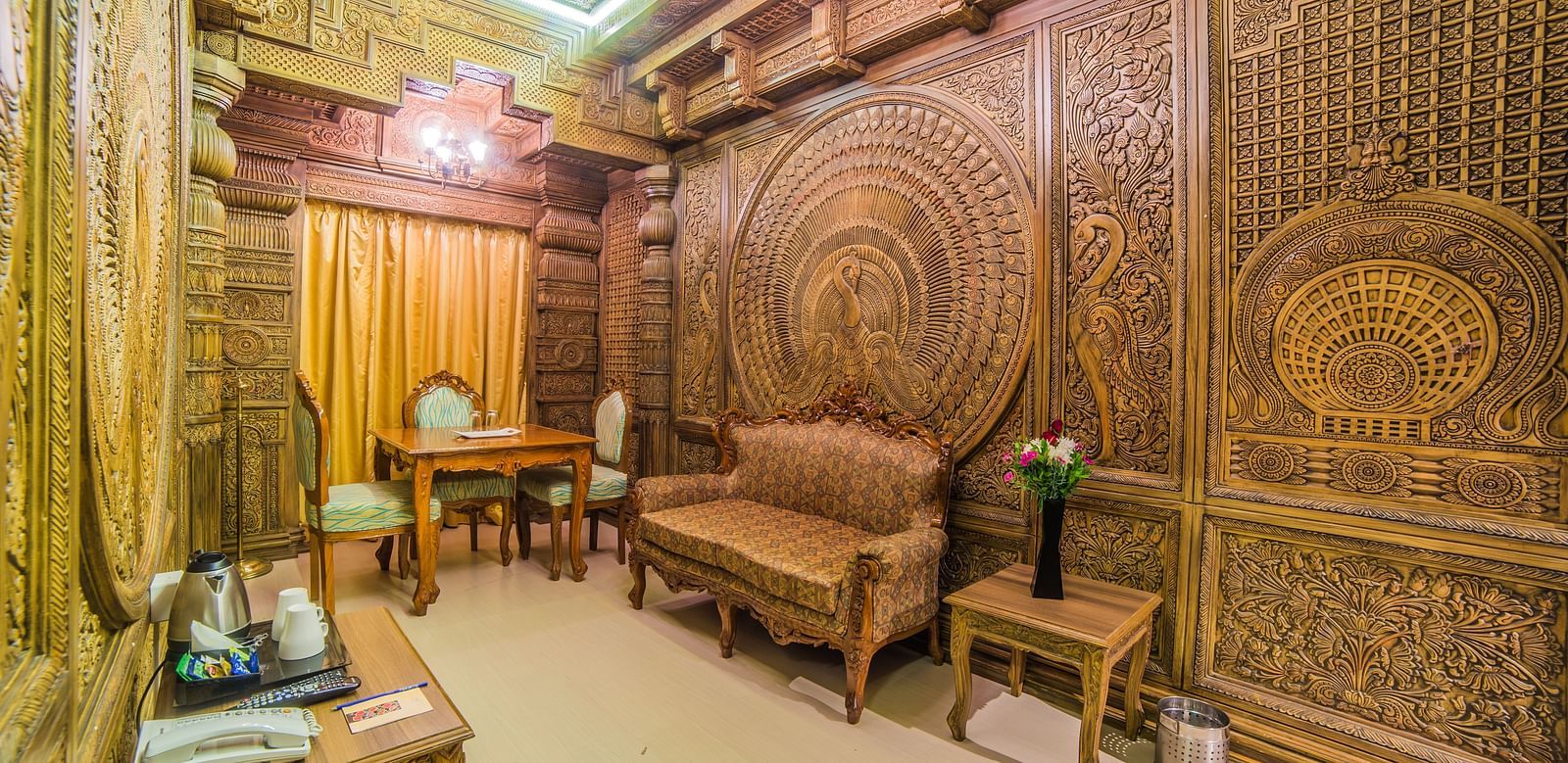 A spacious seating area with ornate wood carvings and classic furniture A grand hotel suite with an opulent red and white decor, large bed, and seating area, reflecting a traditional style at Sitara Luxury Hotel in Hyderabad near Ramoji Film City.