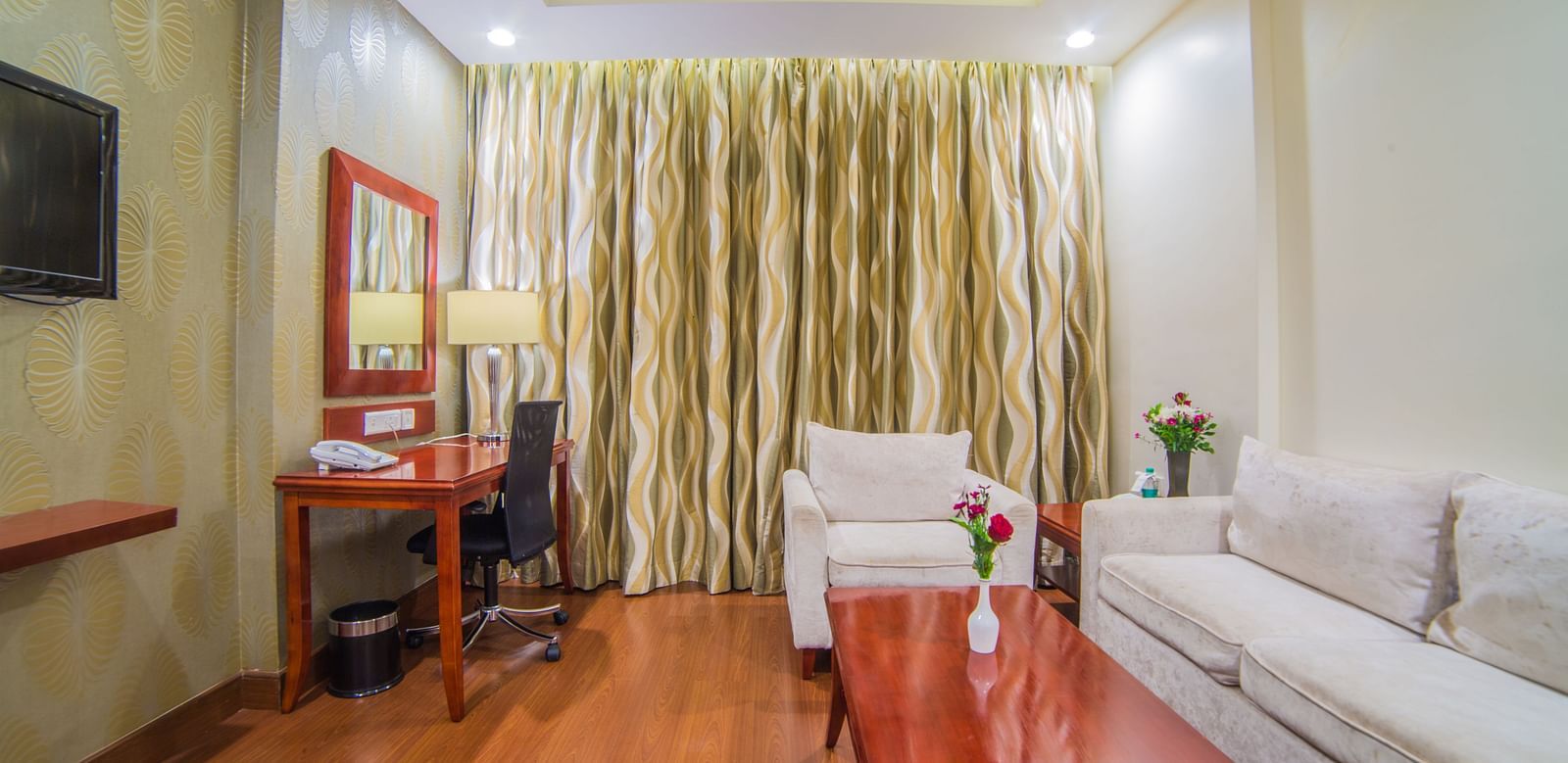 A hotel room with a clean, modern design, featuring a white sofa, work desk, and warm lighting A grand hotel suite with an opulent red and white decor, large bed, and seating area, reflecting a traditional style at Sitara Luxury Hotel in Hyderabad near Ram