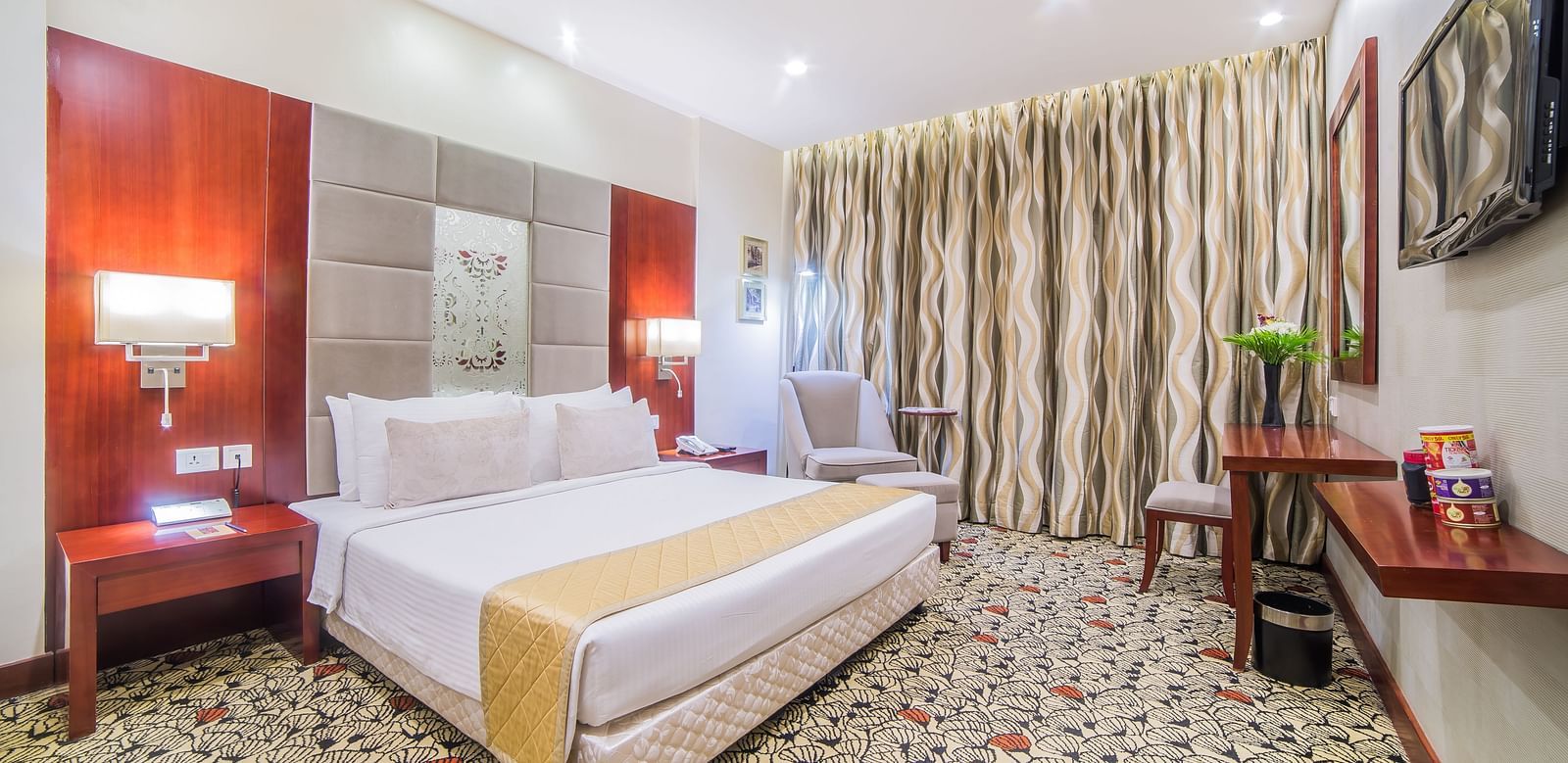 A spacious hotel room with crisp white bedding, a work desk, and tasteful deco A grand hotel suite with an opulent red and white decor, large bed, and seating area, reflecting a traditional style at Sitara Luxury Hotel in Hyderabad near Ramoji Film City.