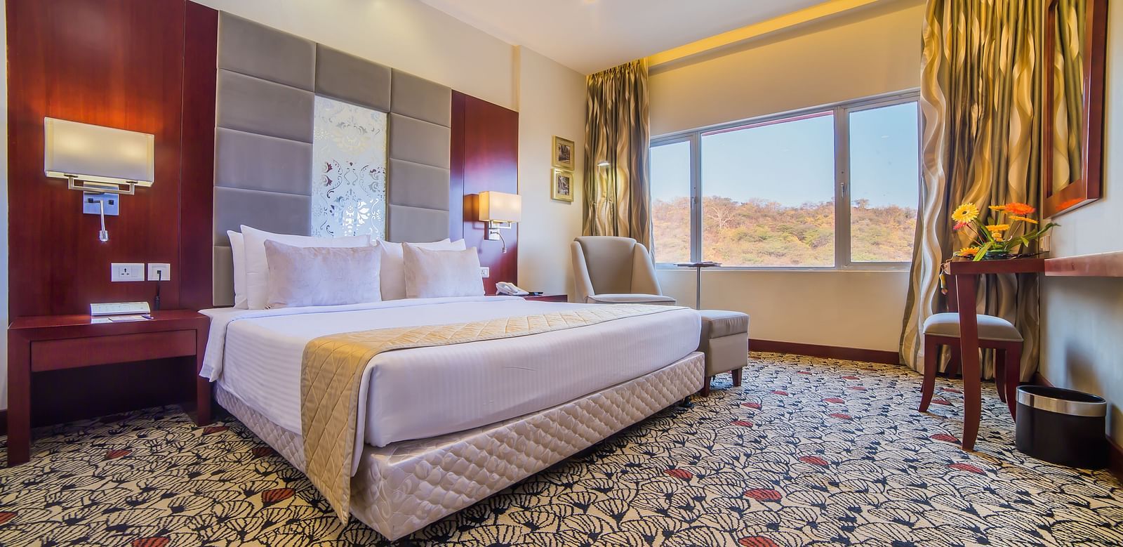 A luxurious hotel room with a plush white bed, warm accent lighting, and a scenic window view A grand hotel suite with an opulent red and white decor, large bed, and seating area, reflecting a traditional style at Sitara Luxury Hotel in Hyderabad near Ramo