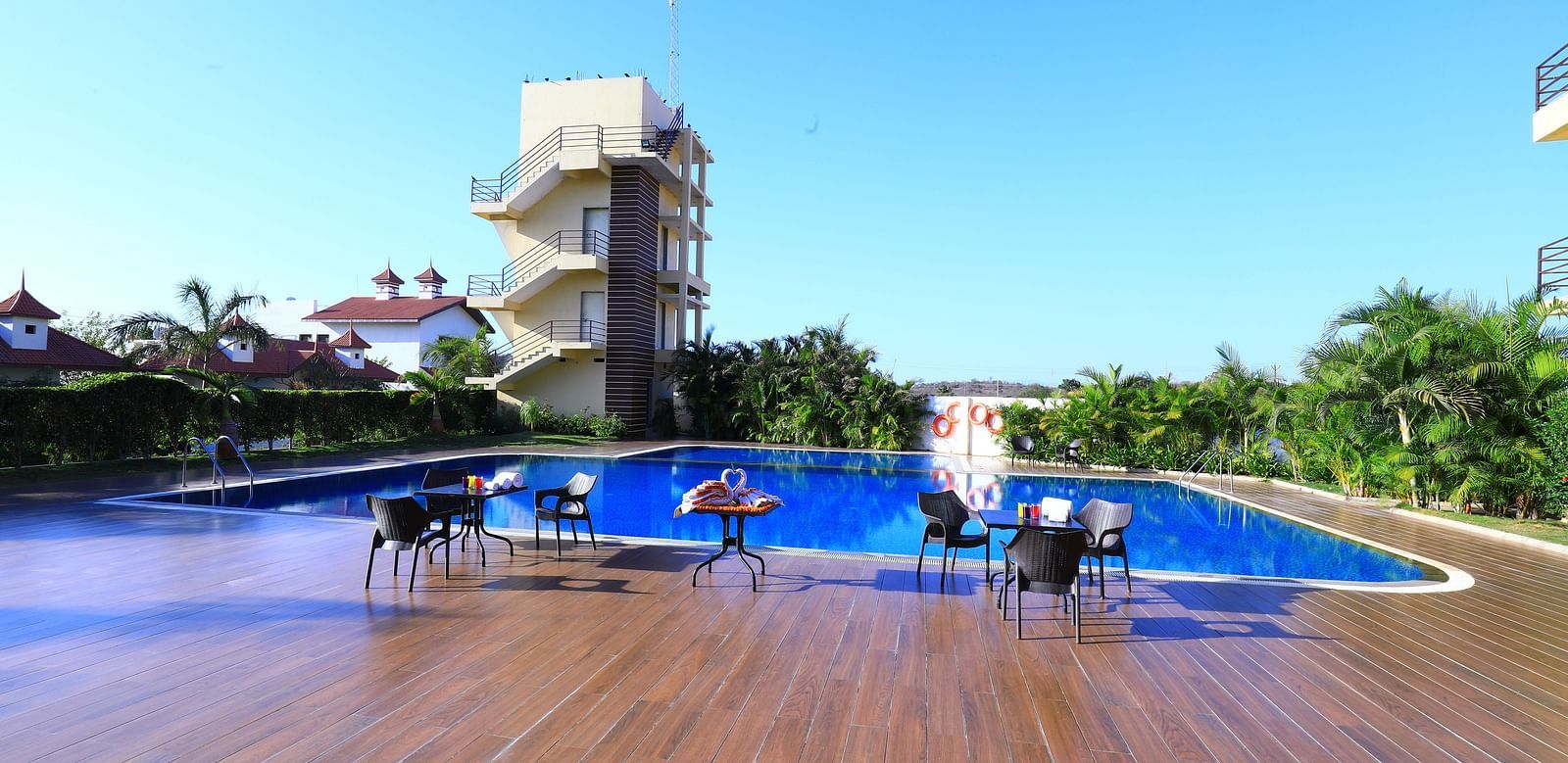 A large swimming pool with sun loungers and umbrellas, surrounded by greenery - Vishal Lords Inn Gir Forest