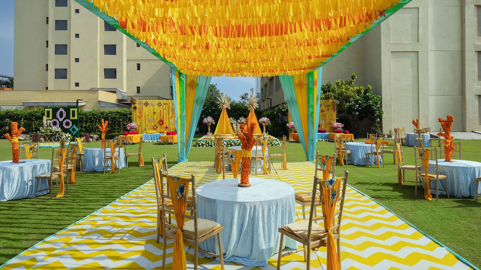two tables with chairs in a cluster seated underneath a canopy during a sunny afternoon for shade - The Hideaway Banquets & Lawns, Greater Noida