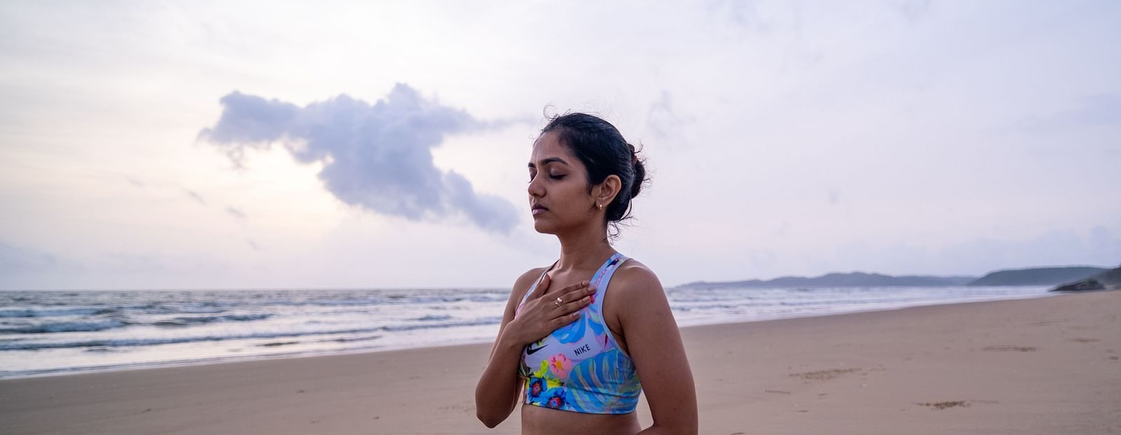 A woman sitting beside an ocean in a yoga pose