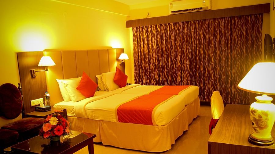 Hotel Yasodha Towers - Interior view of a bedroom containing a queen size bed illuminated with yellow coloured lamps 
