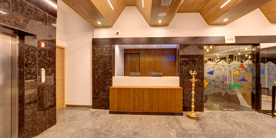 A wooden reception desk, an elevator, and a wooden slatted ceiling in the lobby of Icon Express By Bhagini, Mahadevapura.