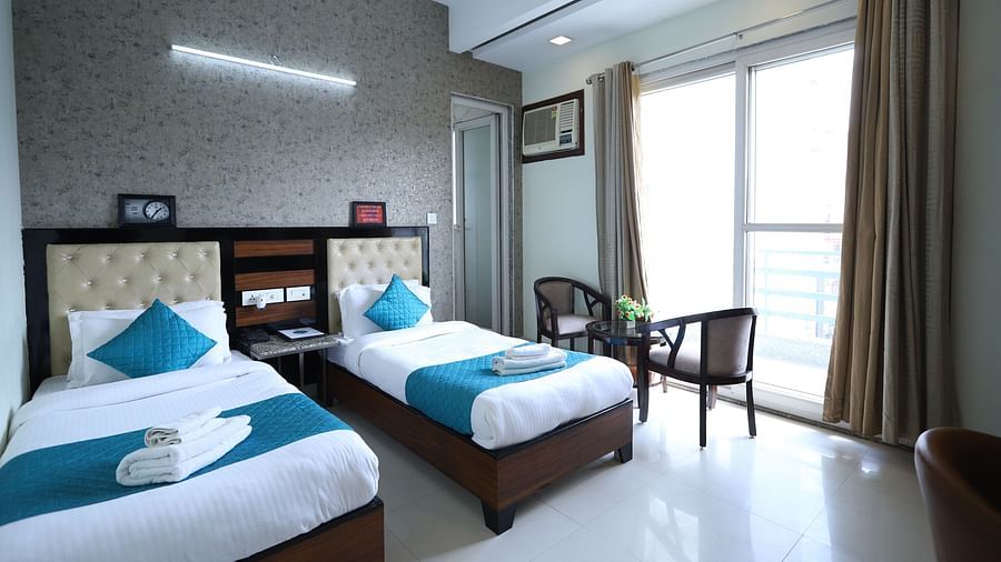 A comfortable room contains two single beds with blue accents, dark furniture, and a window with curtains - Asian Suites Cyber Park, Gurgaon