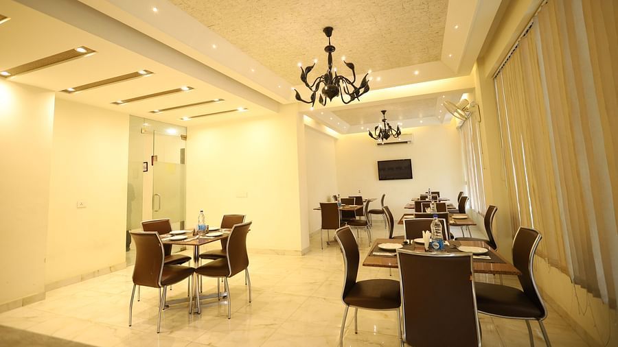 A brightly lit dining area features multiple tables with chairs and modern chandeliers hanging from the ceiling - Asian Suites Cyber Park, Gurgaon