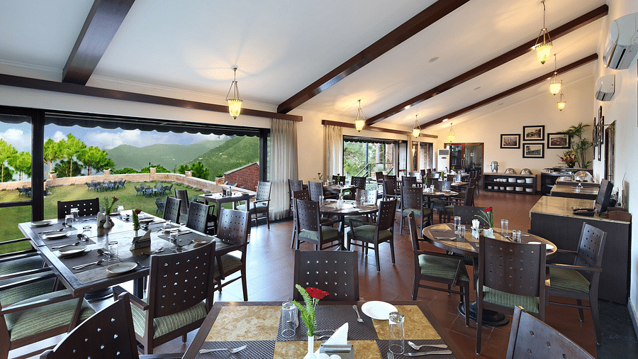 An image of a Restaurant area with wooden chairs and tables which has plates and cutlery on top At baikunth Resort, Kasauli