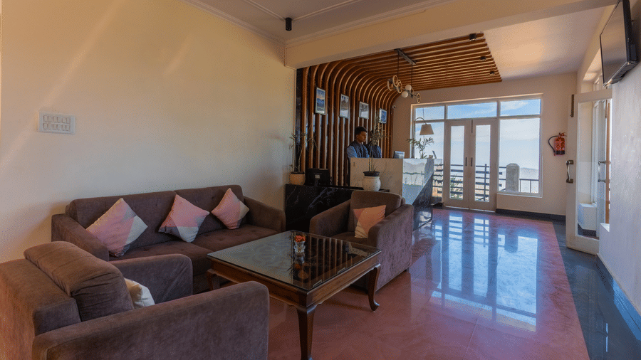 A welcoming reception lounge with plush grey sofas, pink cushions, and a polished floor leading to the desk at Himalayas Resort By The Lake Hill, Mukteshwar.