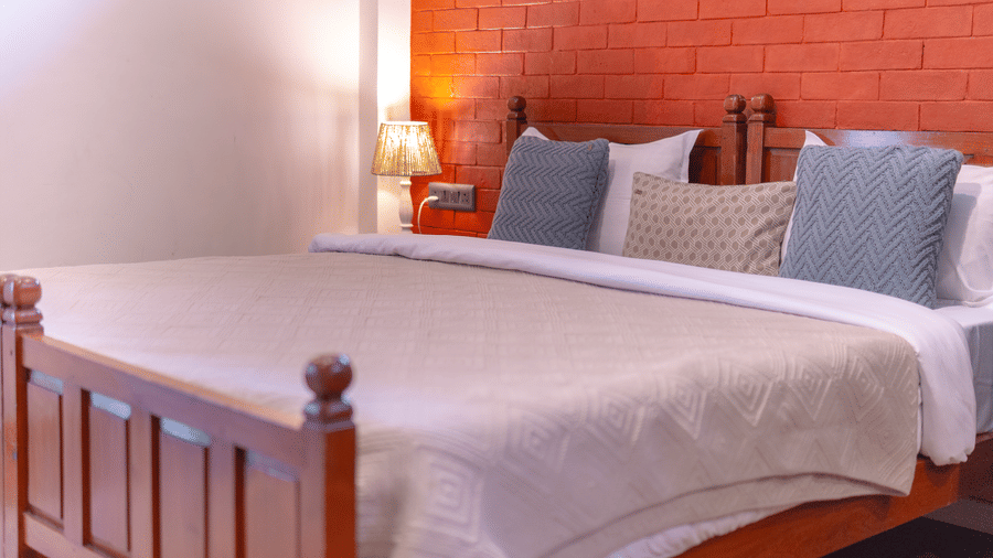 A double bedroom featuring a wooden bed frame, white linens, and a rustic red brick accent wall - Johnson Lodge & Spa, Manali