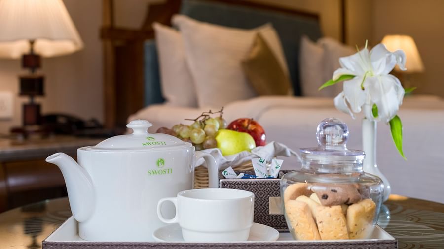 A table arranged with a tray featuring cups, a kettle, a vase of flowers, and some snacks.