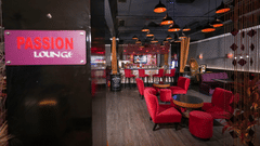 Interior of Passion Lounge at Park Plaza Ludhiana featuring red upholstered seating dark wooden flooring a glowing pink neon sign and warm ambient ceiling lighting.
