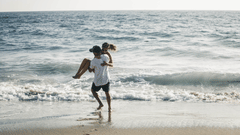 a couple having fun at the beach while the man has lifted the woman i his arms with the cool breeze brushes through their hair
