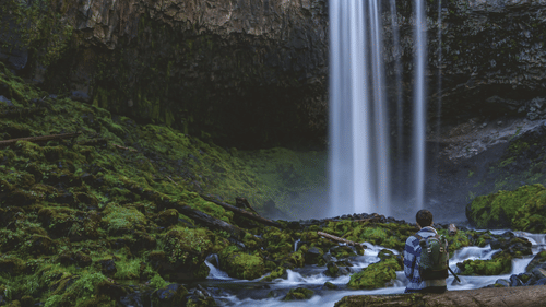 a person sitting on a boulder looking at a waterfall in the distance