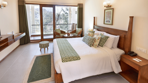 Deluxe room featuring a fluffy bed, beside table, sitting area with sofa chairs and a centre table. This room at Suryavilas Luxury Resort and Spa also has a balcony attached.