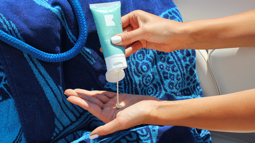 A person applying sunscreen on their hands before a water activity.
