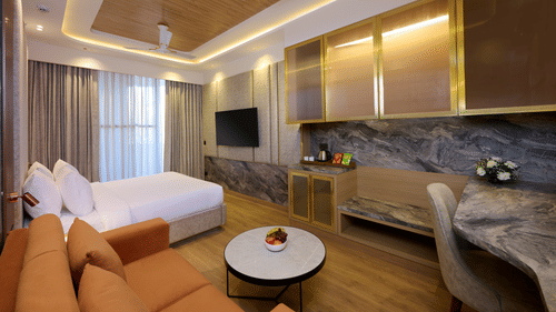 Living area and bedroom combo at Tulip Inn Gurugram with a marble-topped coffee table, a couch, and integrated storage units.