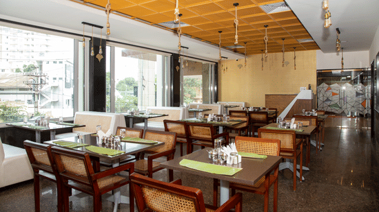 Seating area in the dining hall featuring large windows, multiple tables, and wooden chairs, at Icon Express By Bhagini, Mahadevapura.