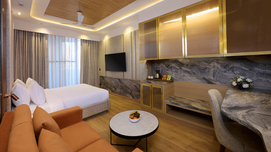 Living area and bedroom combo at Tulip Inn Gurugram with a marble-topped coffee table, a couch, and integrated storage units.