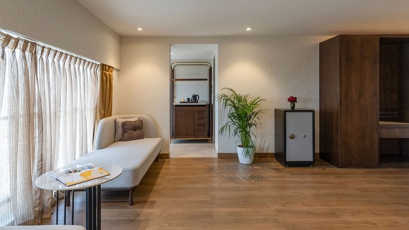 Stylish lounge zone with light wood floors, potted plant, chaise, mini fridge, and view towards the bathroom area at Clarks Inn Suites, Hyderabad