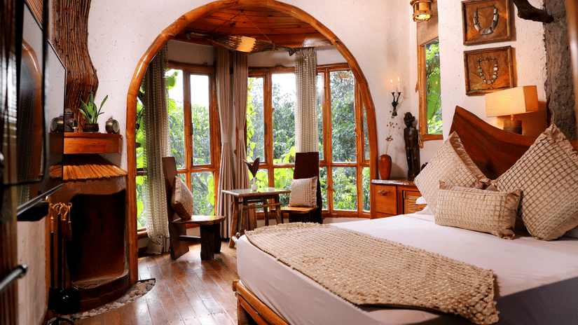 A bedroom with  a queen bed and an arc pass through leading to the sitting area overlooking the greenery at  The Den Corbett Resort and Spa.