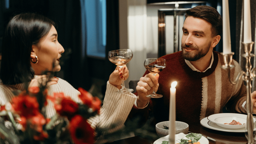 A couple looking at each other and holding their glasses up while being seated on a candlelight dinner