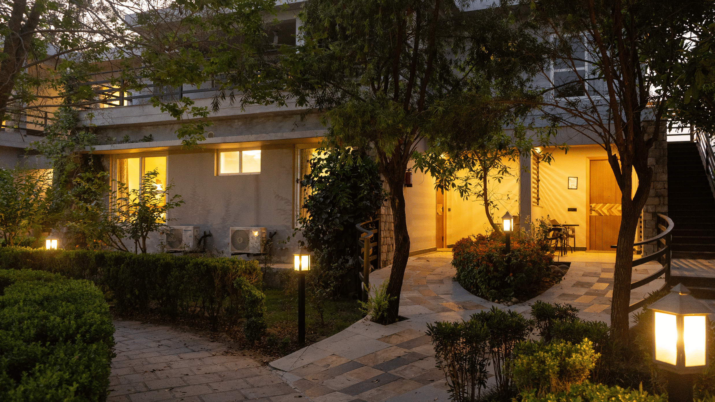 Building's exterior illuminated with warm lights, showing a pathway and garden area at The Golden Tusk, Jim Corbett