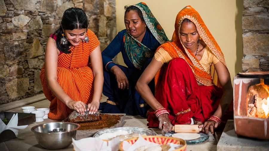An image of three women in the kitchen, where one is cooking, one is grinding condiments, one woman is making roti- Juna Mahal Jungle Resort, Ranthambore