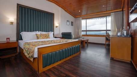 Premium Valley View Room at Summit North Star, Gangtok featuring a bed, a cabinet table, a seating area, and a large window with valley view.