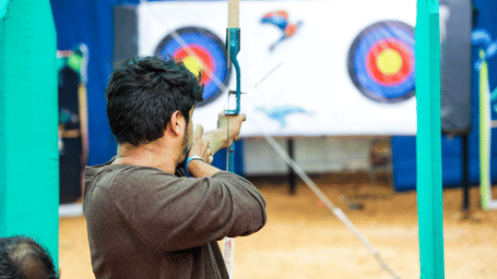 A man aims his bow towards a large archery target on an outdoor range - District Gravity Adventure Park, Hyderabad