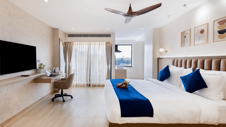 A bedroom at Sunrise A Boutique Hotel, Kondapur featuring 2 king size beds, a desk with a chair, a wall-mounted TV, a ceiling fan, bedside lamps, and a window with curtains.