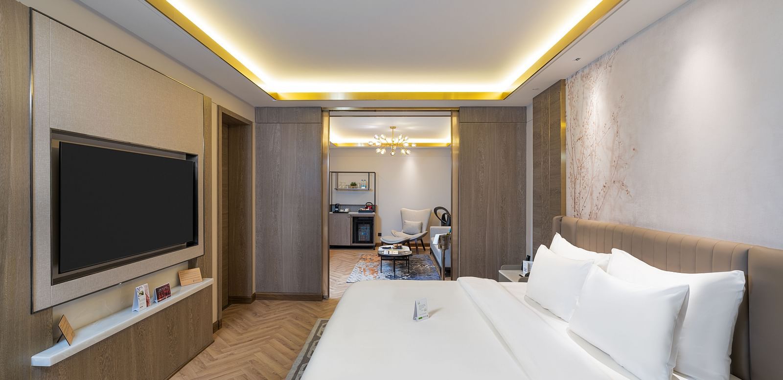 Nirvana Suite bedroom featuring a bed, wall-mounted TV, subtle ambient lighting, and a glimpse into the suite layout - Nirvana Luxury Hotel, Ludhiana