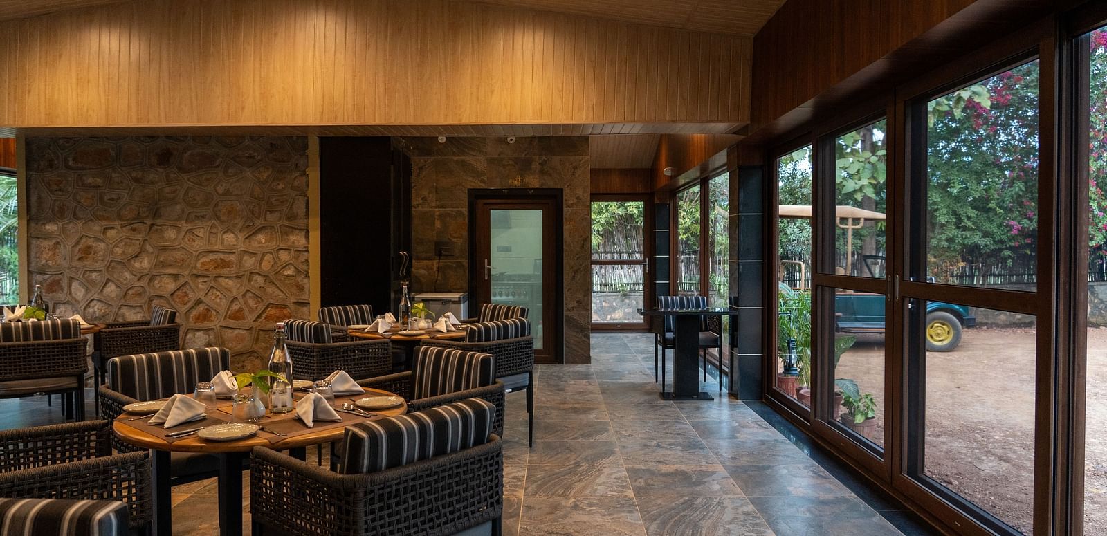 A stylish indoor dining area at Aamaghati Jungle Retreat Ranthambore with large glass doors and set tables.