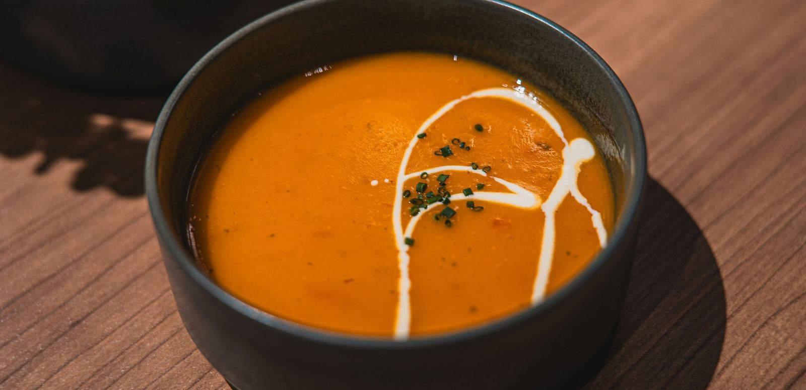 A bowl of creamy tomato soup garnished with herbs and a swirl of cream.